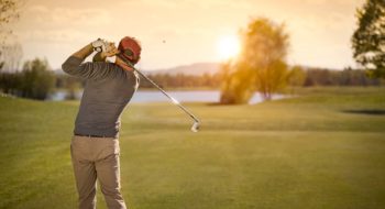 Man drives golf ball at dusk