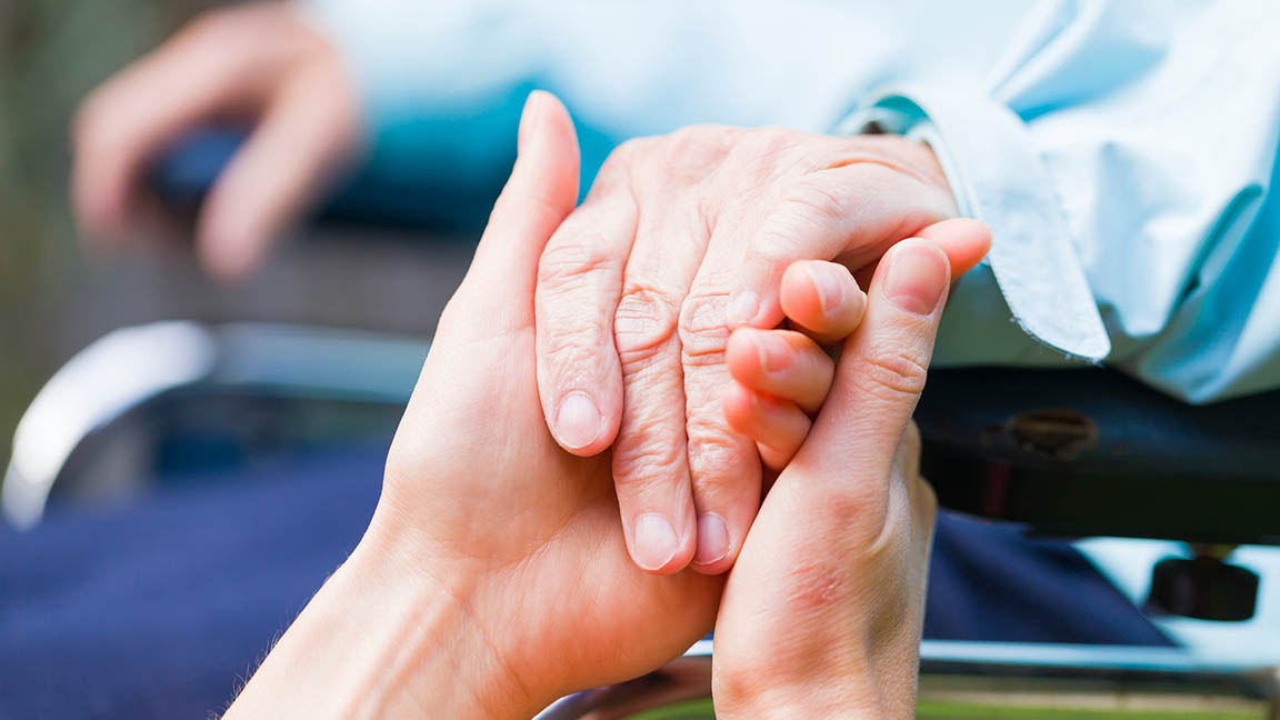 Caregiver holds a patient's hand.