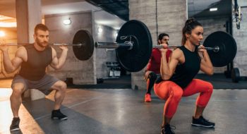 Two young men and a woman lifting weights at the gym.