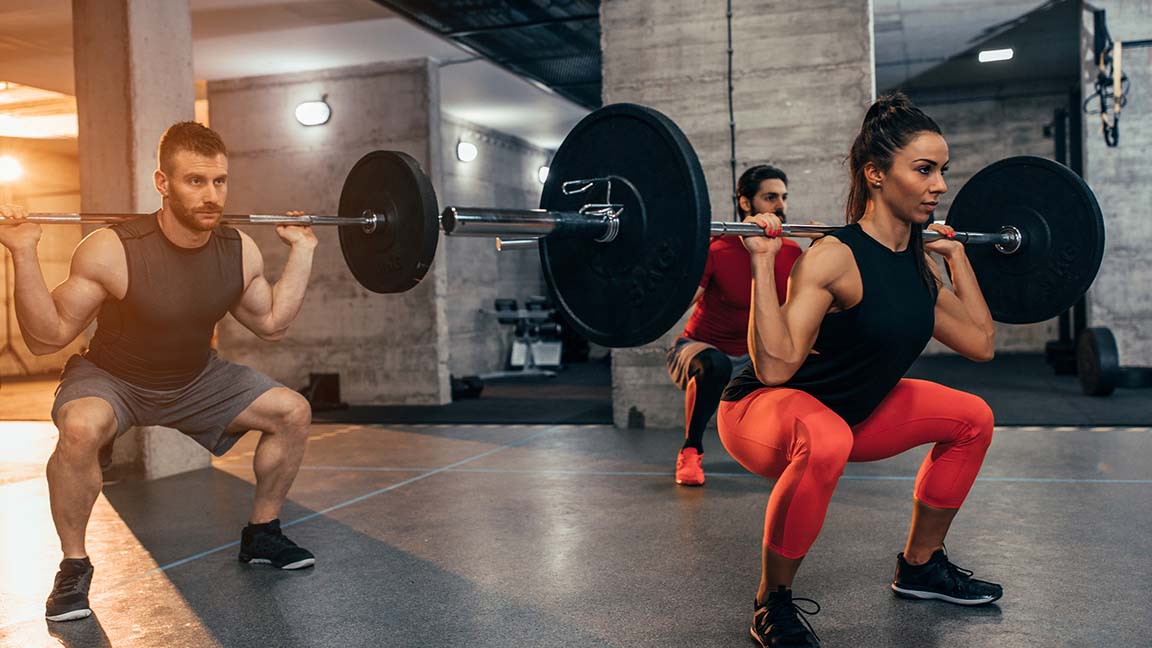 Two young men and a woman lifting weights at the gym.