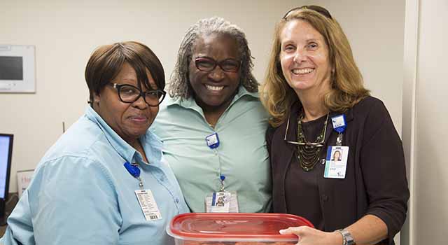Beth Ward, executive vice president and chief financial officer for Tidelands Health, at right, delivers a container of freshly baked, homemade chocolate chip cookies to Tidelands Health team members fielding phone calls and helping keep patient records.