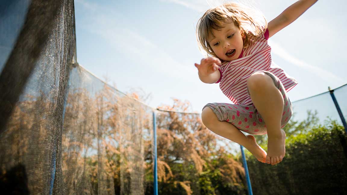 Child jumping high on big trampoline outside in garden