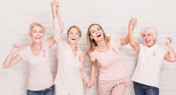 Group of smiling ladies with pink ribbons cheering and holding hands