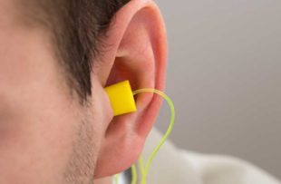 Close-up Of Yellow Earplug Into The Ear Of Person