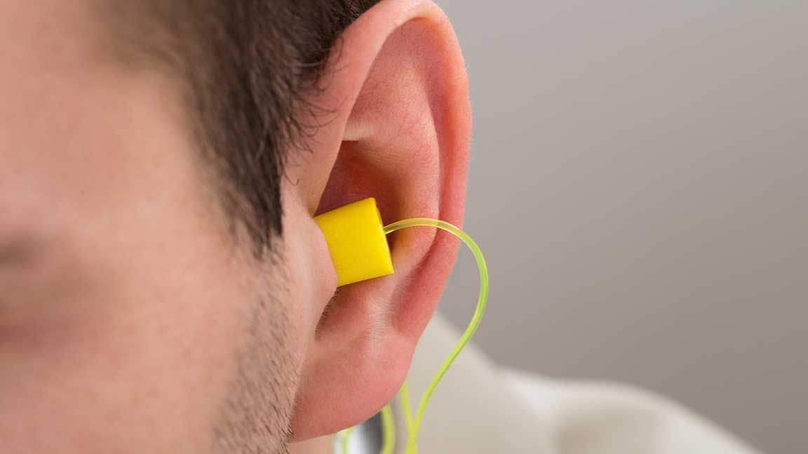 Close-up Of Yellow Earplug Into The Ear Of Person
