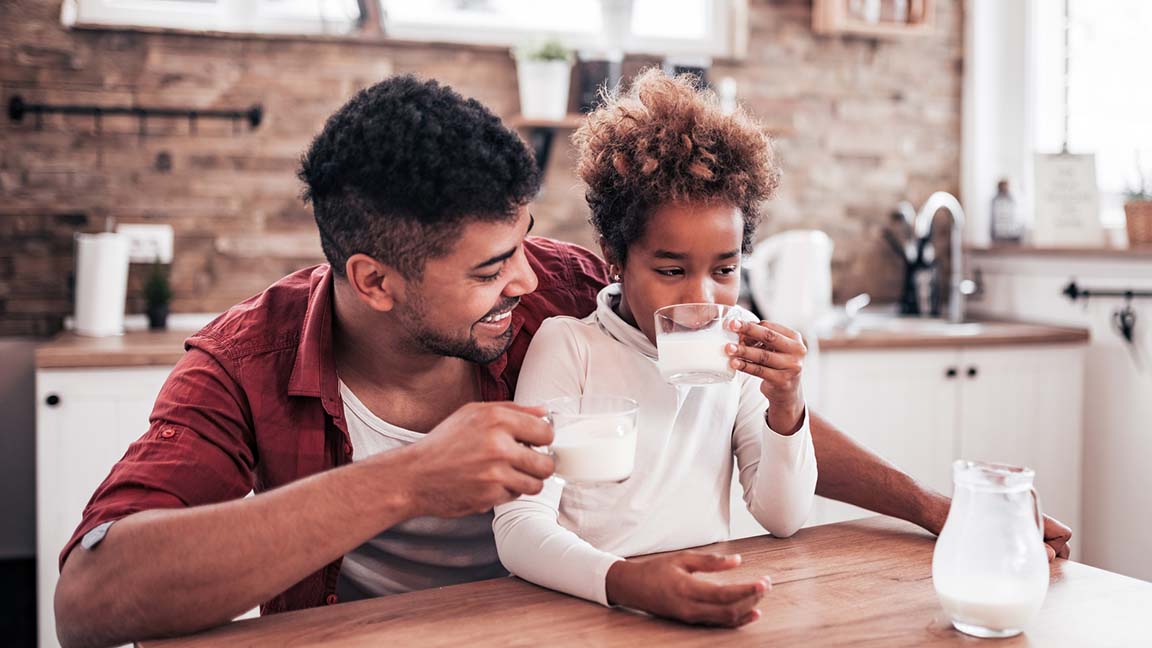 Little girl and her father drinking milk at the kitchen table.