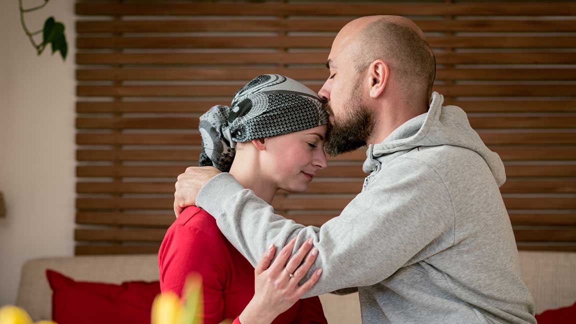 Supportive husband kissing his wife, cancer patient, after treatment in hospital. Cancer and family support concept.