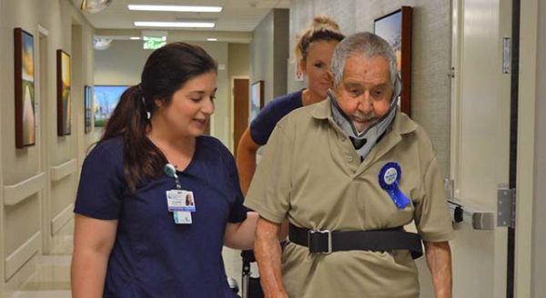 Patient Oscar Sanchez walks the hallway at Tidelands Health Rehabilitation Hospital, an affiliate of Encompass Health, on Saturday to his 100th birthday party with the help of occupational therapists Julianna Brown, left, and Karla Ehlers.