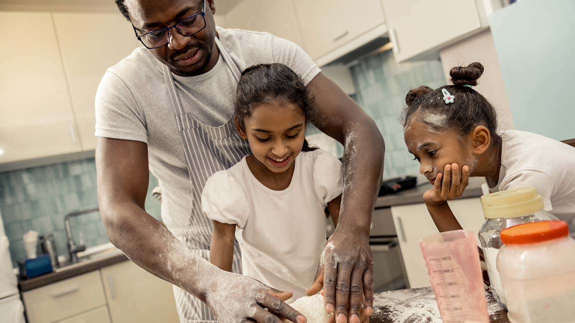 Father teaches daughters how to cook.