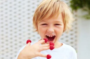 Delighted boy eating raspberries