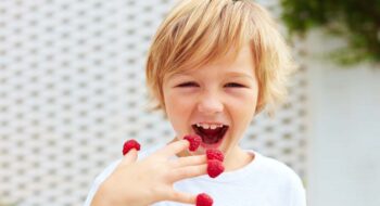 Delighted boy eating raspberries