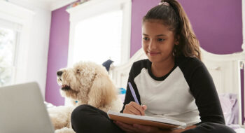 Young teen girl studying on her bed beside pet dog