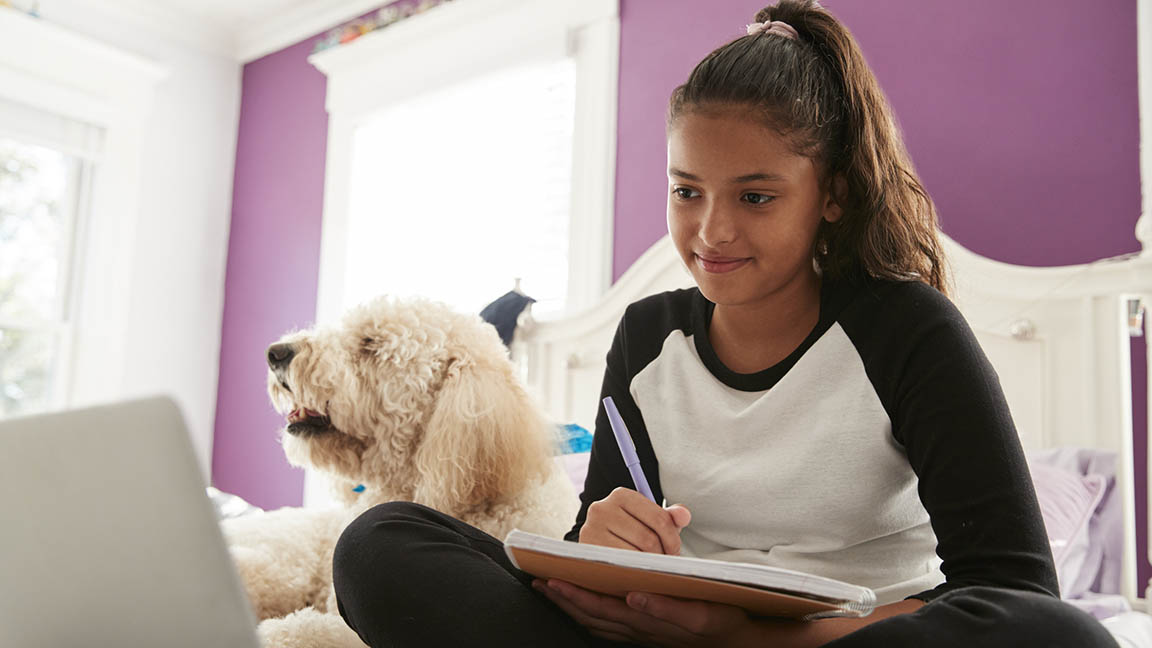 Young teen girl studying on her bed beside pet dog