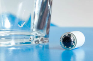 Capsule with camera for capsular endoscopy and glass of water on blue surface