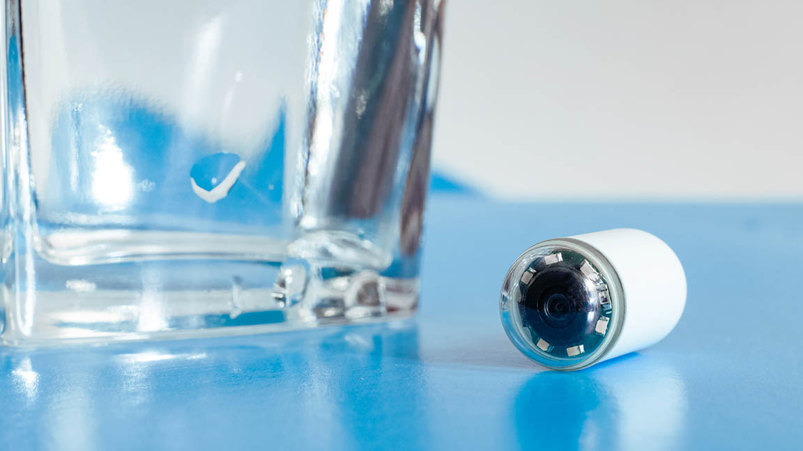 Capsule with camera for capsular endoscopy and glass of water on blue surface