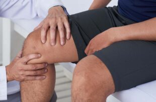 Doctor checking knee of male patient
