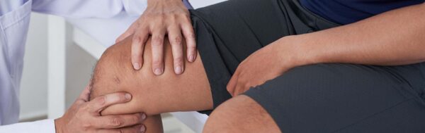 Doctor checking knee of male patient