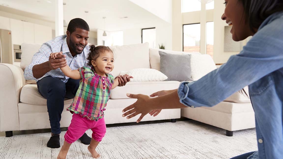 Family At Home Encouraging Baby Daughter To Take First Steps