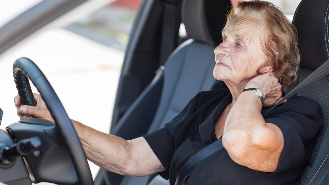 Senior woman driving with neck pain.