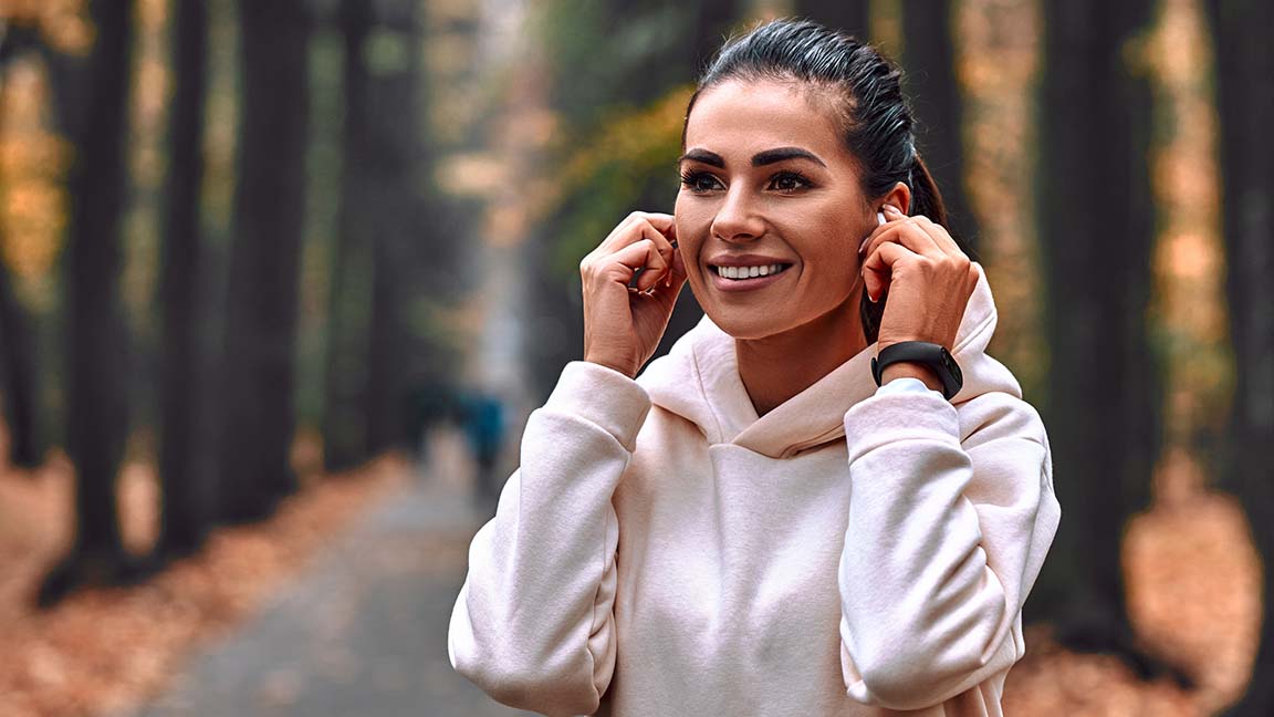 Morning autumn jog. Young woman adjusts headphones before jogging.