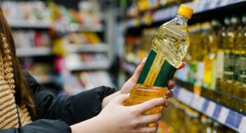 Woman choosing sunflower oil in the supermarket. Close up of hand holding bottle of oil at store.