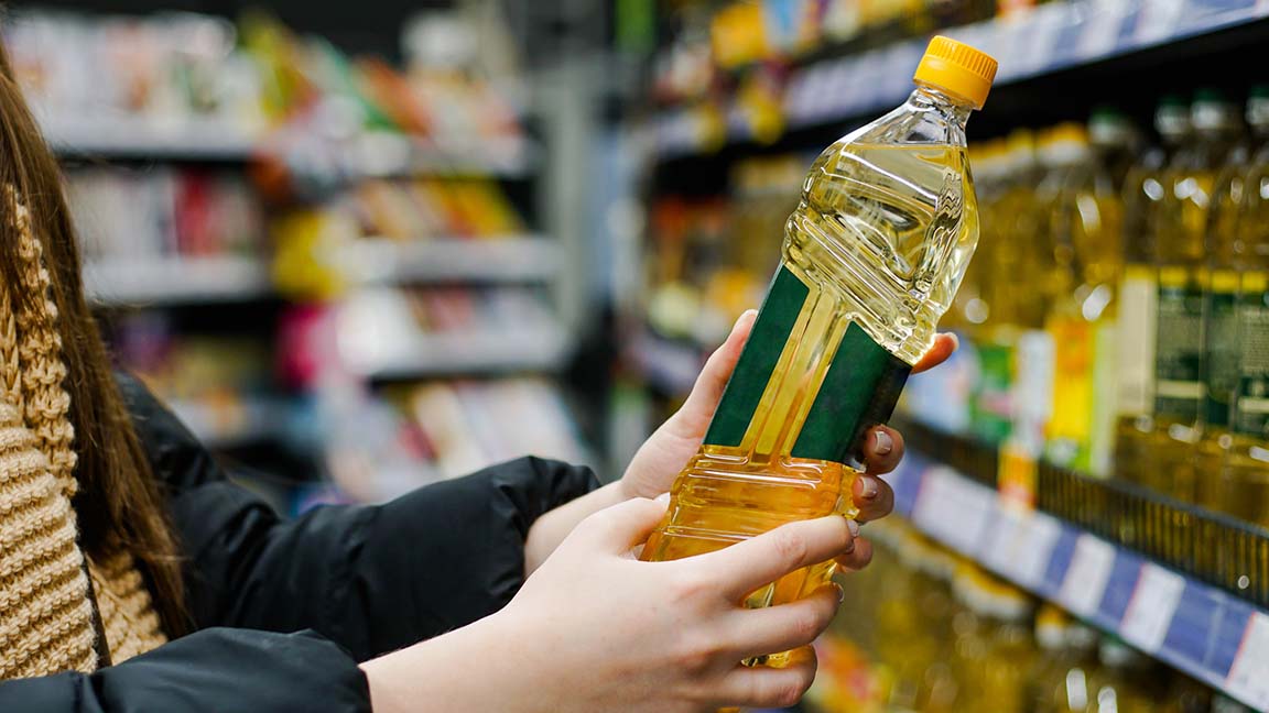 Woman choosing sunflower oil in the supermarket. Close up of hand holding bottle of oil at store.