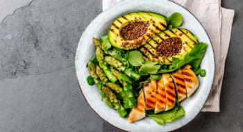 Healthy grilled chicken, grilled avocado and asparagus salad with linen seeds. Balanced lunch in bowl. Gray slate background. Top view.