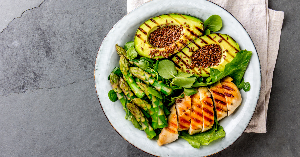 Healthy grilled chicken, grilled avocado and asparagus salad with linen seeds. Balanced lunch in bowl. Gray slate background. Top view.