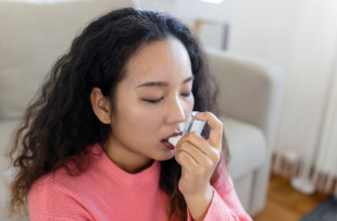 Young woman using inhaler while suffering from asthma at home.
