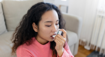 Young woman using inhaler while suffering from asthma at home.