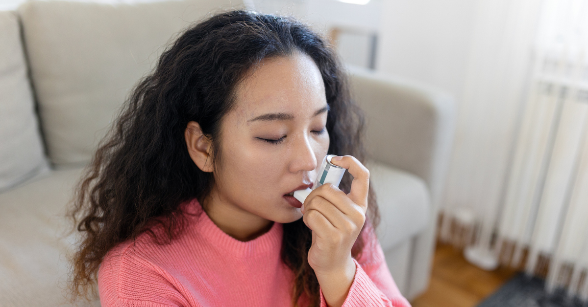 Young woman using inhaler while suffering from asthma at home.