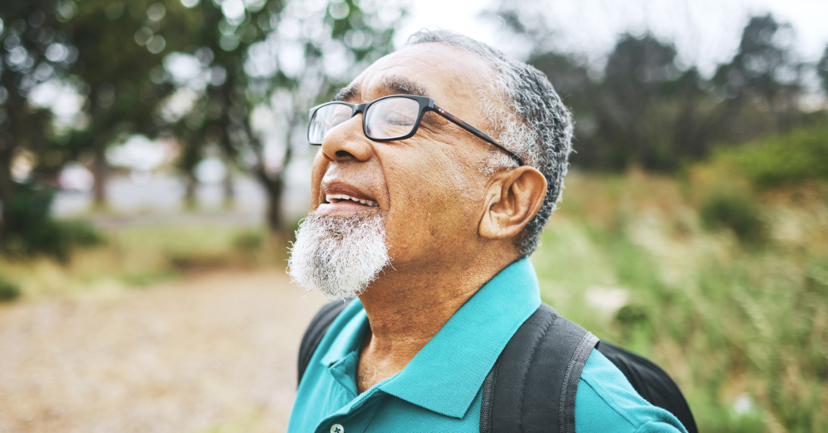 Senior man enjoying the outdoors by breathing deeply on hiking trail.