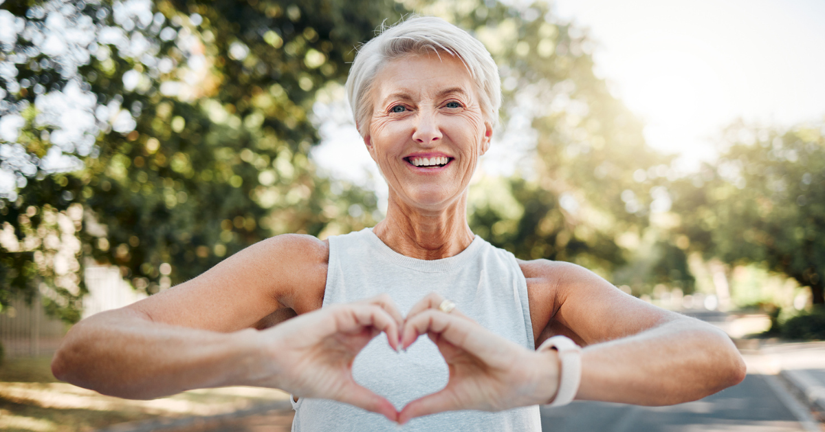 Happy and fit woman in nature after running for health, wellness and workout making a heart with her hands.