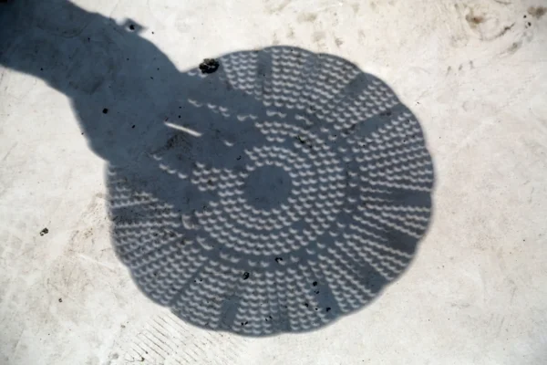 The circular holes of a colander project crescent shapes onto the ground during the partial phases of a solar eclipse.