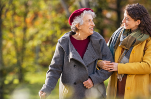 Young woman in park wearing winter clothing walking with old grandmother.