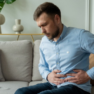 A man suffers from abdominal pain while sitting at home on the couch.