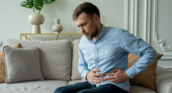 A man suffers from abdominal pain while sitting at home on the couch.