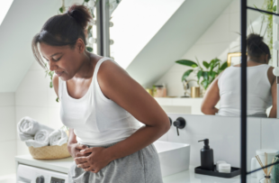 Young woman standing in the bathroom and feeling pain in the stomach area.