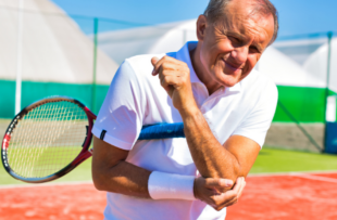 Senior man with elbow pain standing during tennis match on sunny day