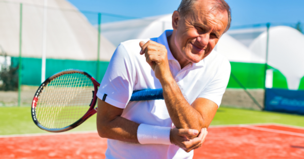 Senior man with elbow pain standing during tennis match on sunny day
