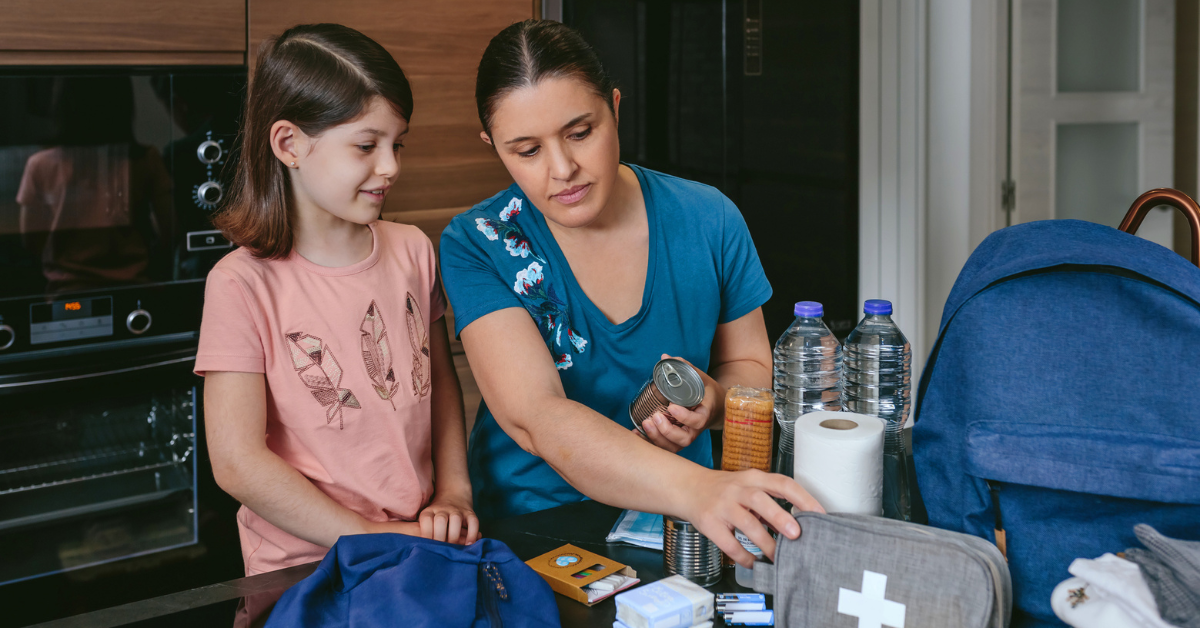 Mother preparing emergency backpack with her daughter in the kitchen