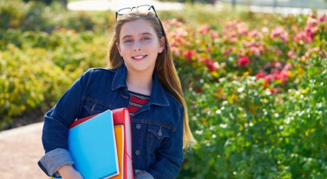 Blond kid student girl with notebook and backpack in the park back to school