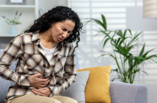 A woman with stomach pain, grabbing her stomach while sitting on the couch.