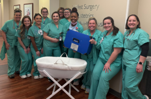 A group of clinical OBGYN clinical staff stand and smile while holding a CuddleCot.