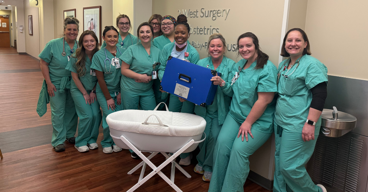 A group of clinical OBGYN clinical staff stand and smile while holding a CuddleCot.