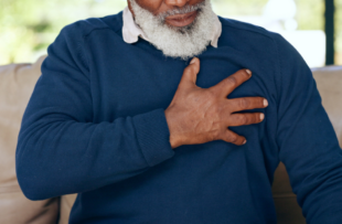 Closeup, senior and chest with heartburn, indigestion or medical emergency of stroke on sofa