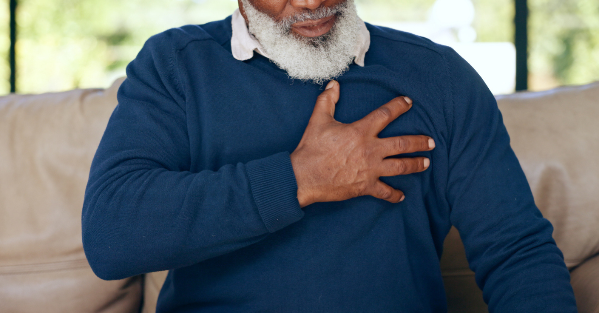 Closeup, senior and chest with heartburn, indigestion or medical emergency of stroke on sofa