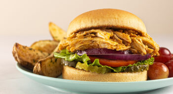 A loaded pulled chicken sandwich with a side of potato wedges and grapes.