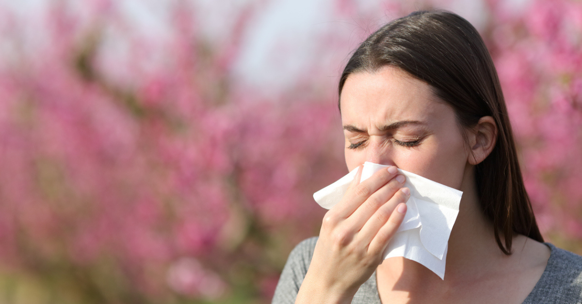 Woman blowing on tissue suffering allergy in spring in a field