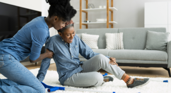 An older woman holding on to her leg after falling on the floor. Being helped by another woman.